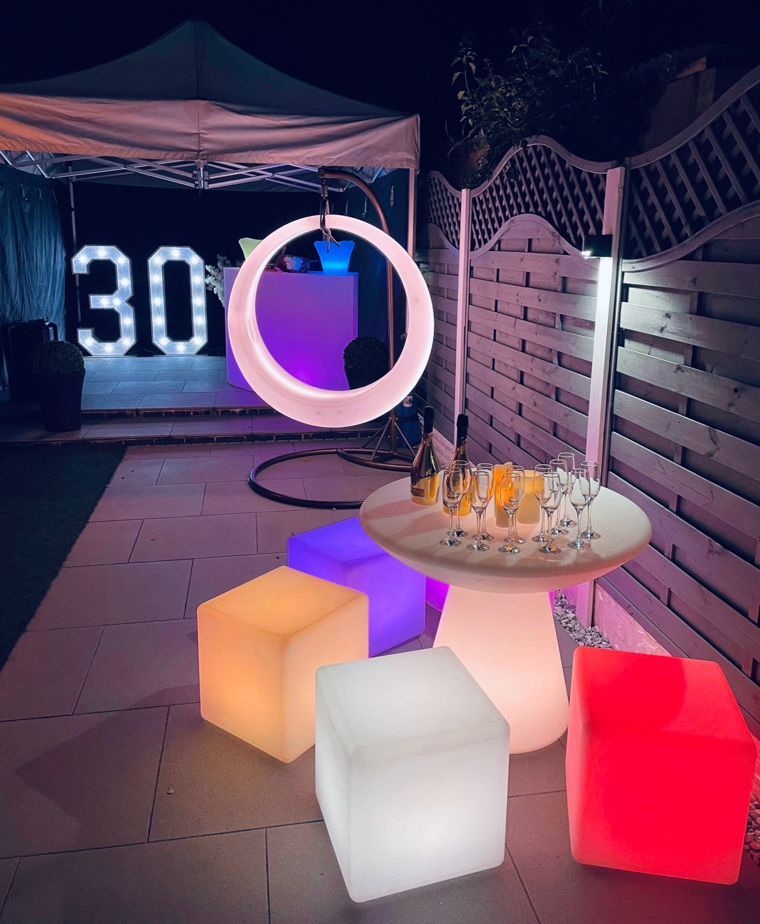 Multi-colour illuminated LED swing with matching glowing party furniture in a garden